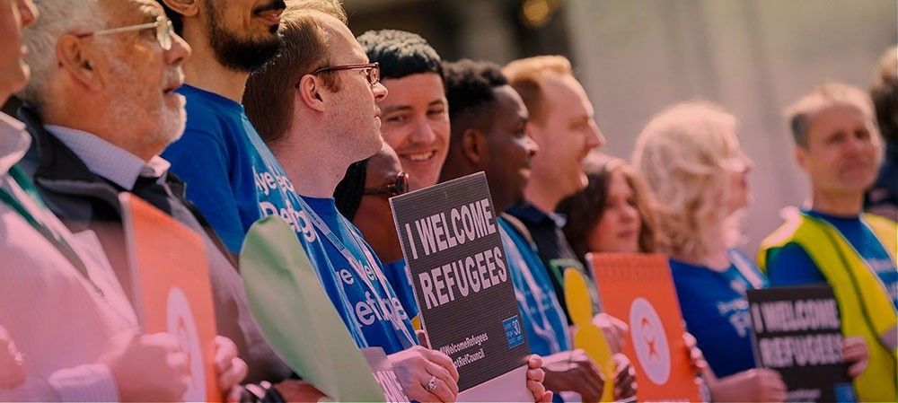 A row of people holding signs saying I welcome Refugees.