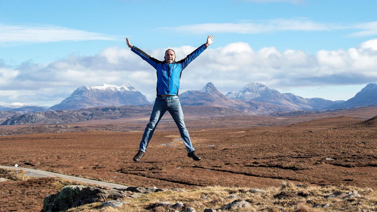 Allan MacFadyen jumping up in front of a mountainous landscape.