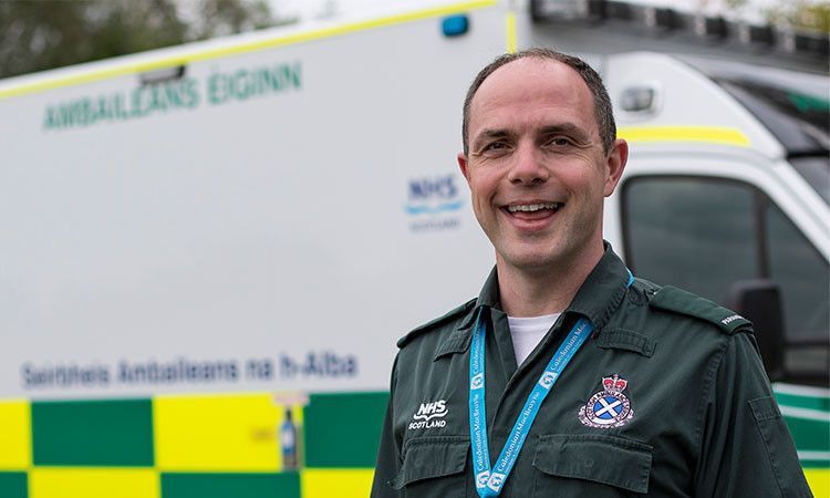 Allan MacFadyen in his green paramedic uniform, standing in front of an ambulance.