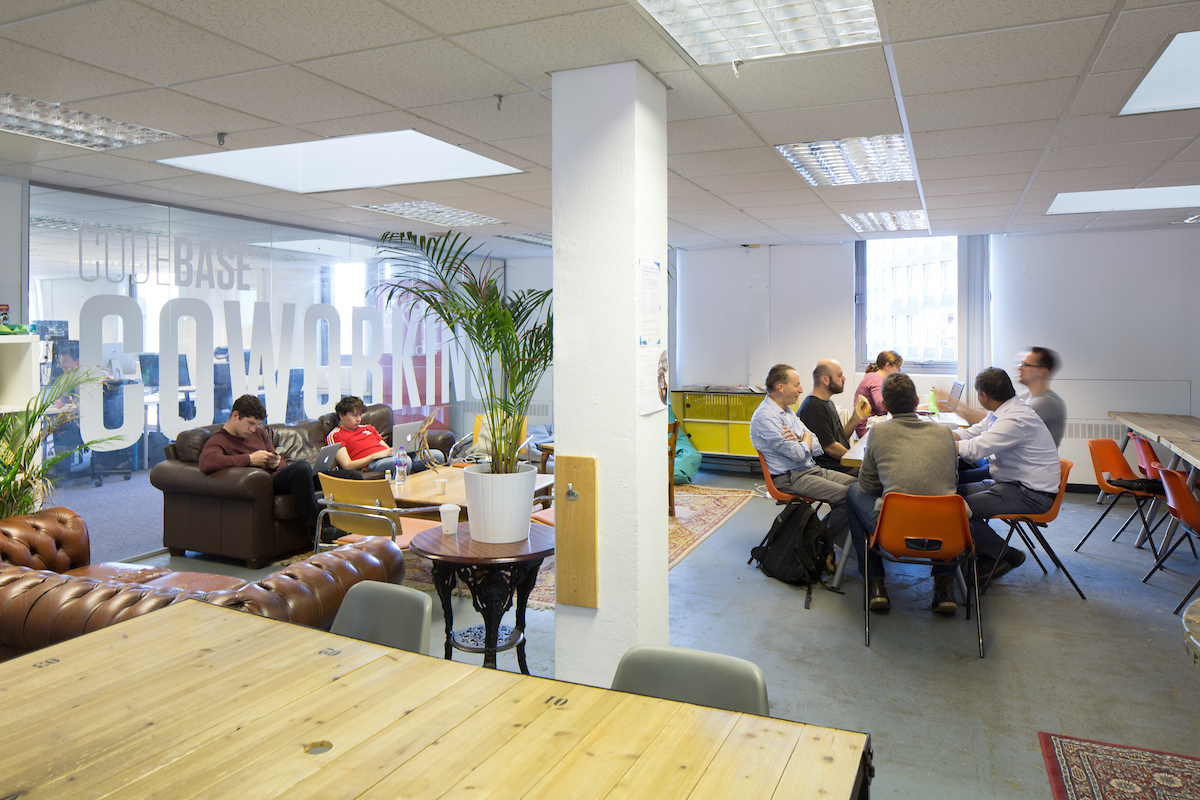 Image of three people working in the CodeBase coworking space at a large communal desk.